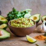 Fresh-guacamole-bowl-with-seasoning-ingredients-like-avocados-lime-garlic-chili-powder-and-cilantro-on-a-wooden-table